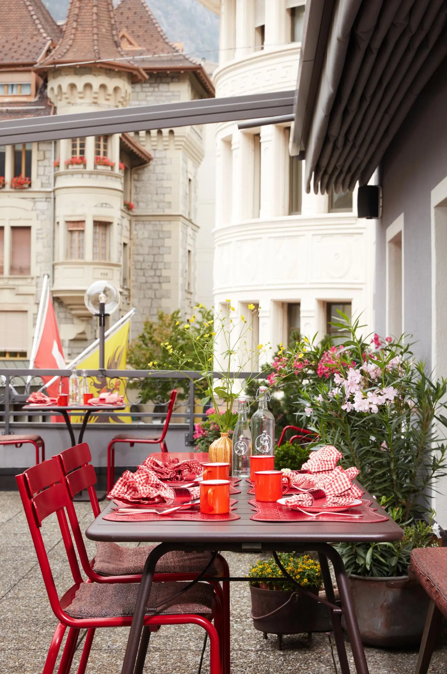 Hotelterrasse mit gedecktem Tisch by Frohsinn von Atelier Zurich, roten Stühlen und Blick auf historische Architektur