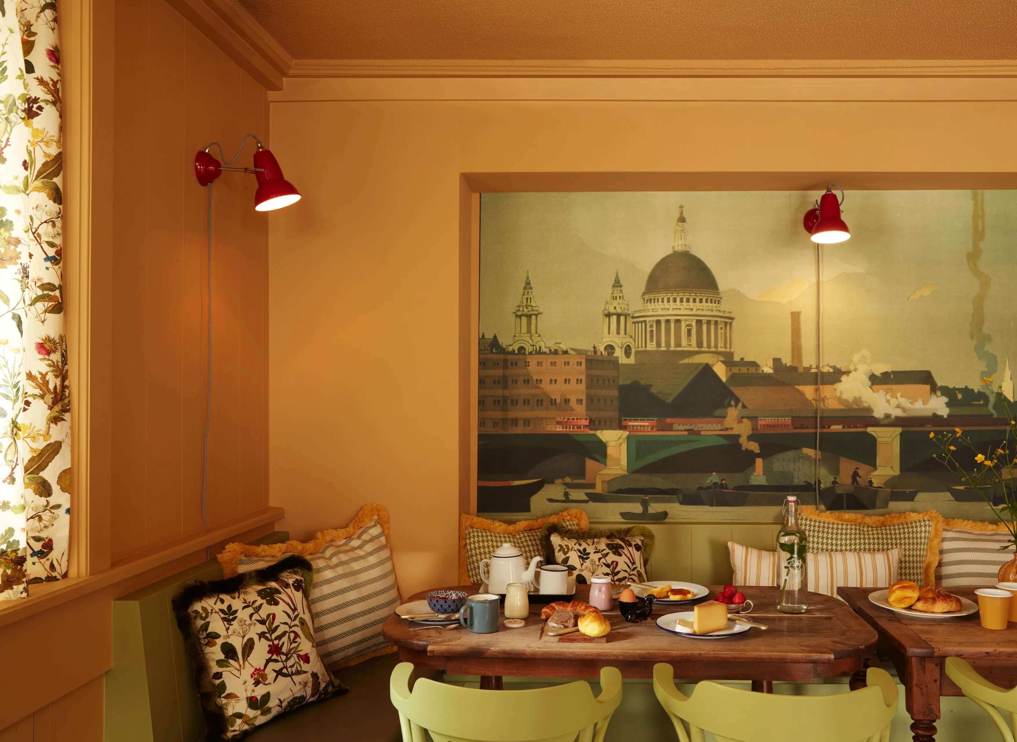Frühstücksbereich im Hotel mit langer Gemeinschaftstafel, Sitzbank und Blick auf die Londoner Skyline