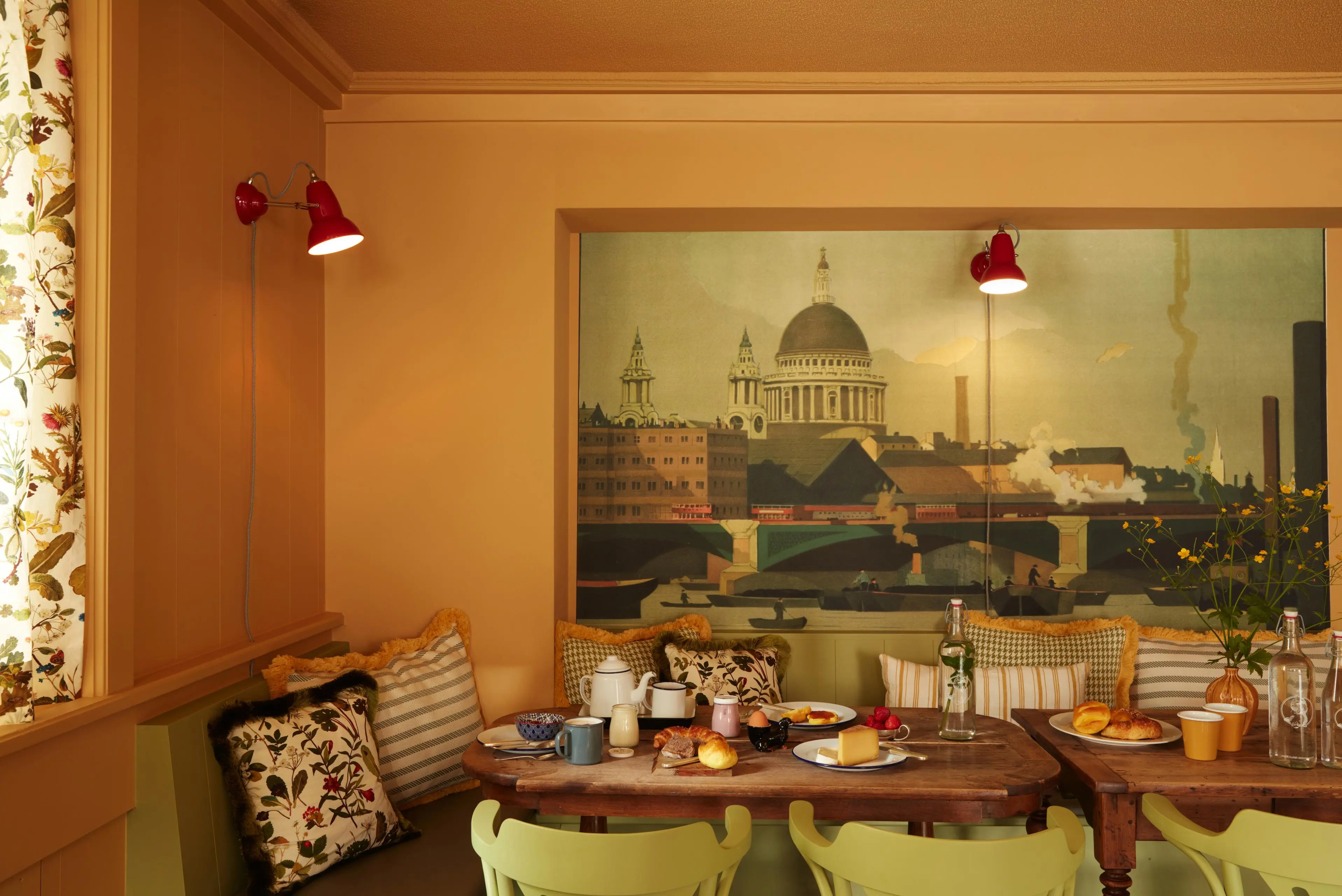 Frühstücksbereich im Hotel mit langer Gemeinschaftstafel, Sitzbank und Blick auf die Londoner Skyline