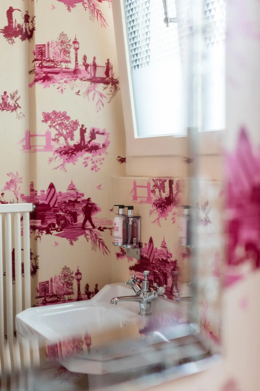 Hotel bathroom with pink Timorous Beasties wallpaper, classic washbasin and chrome fittings